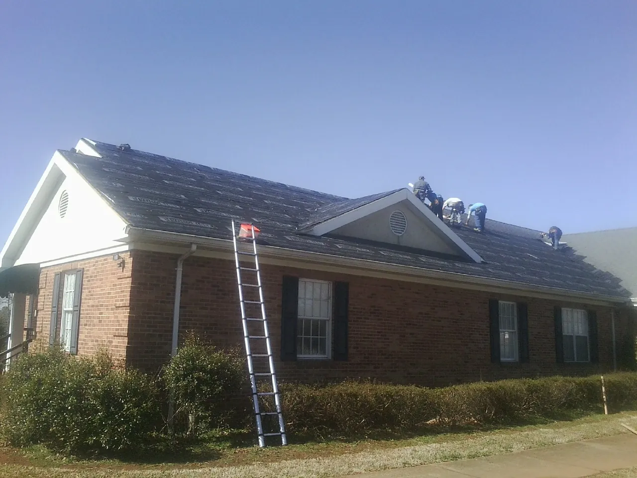 Crew tearing shingles off a brick ranch roof with a ladder set — Metal Roof Repair work by our crew in Steptoe
