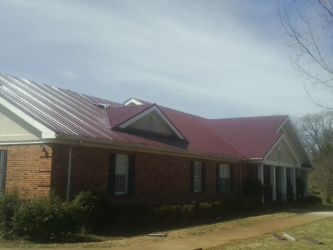 Red metal roof with gabled entries on a long brick building, from a Hail Damage Roof Repair job in Steptoe