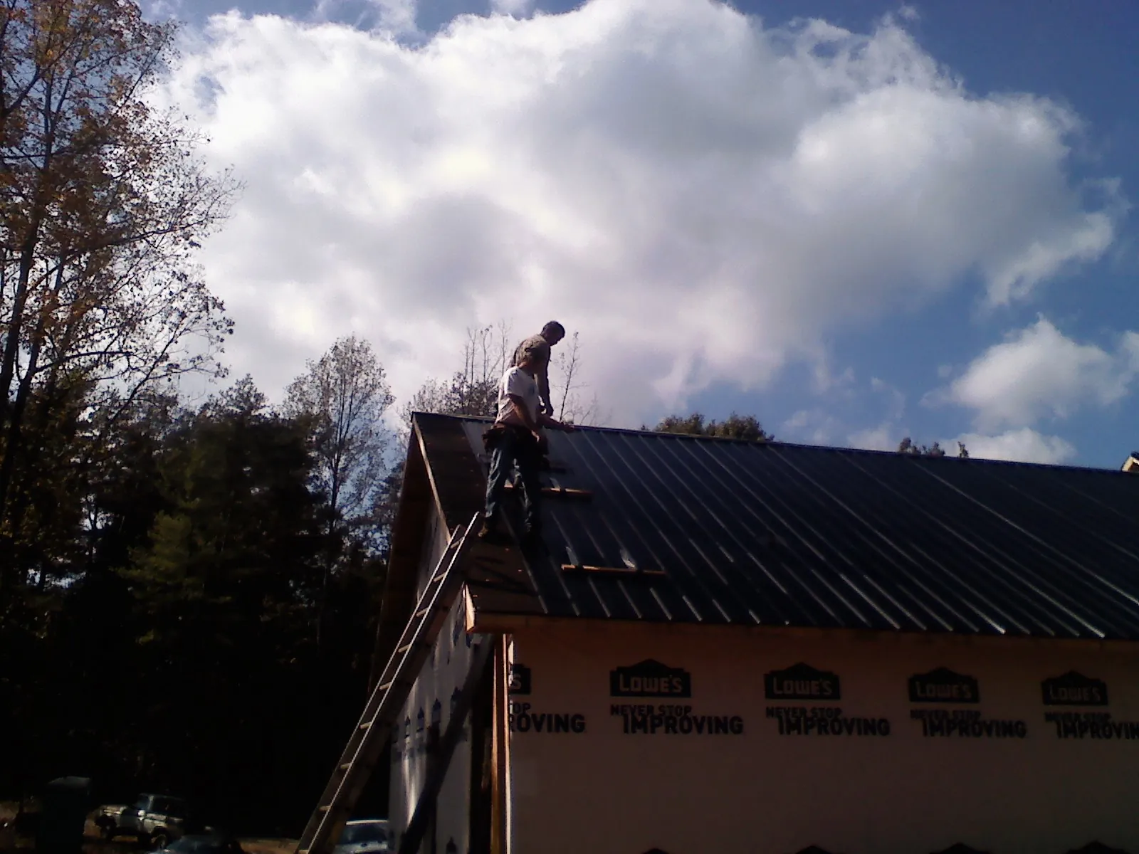 Roofer fastening dark metal panels high against a cloudy sky, from a Roof Inspection job in Steptoe